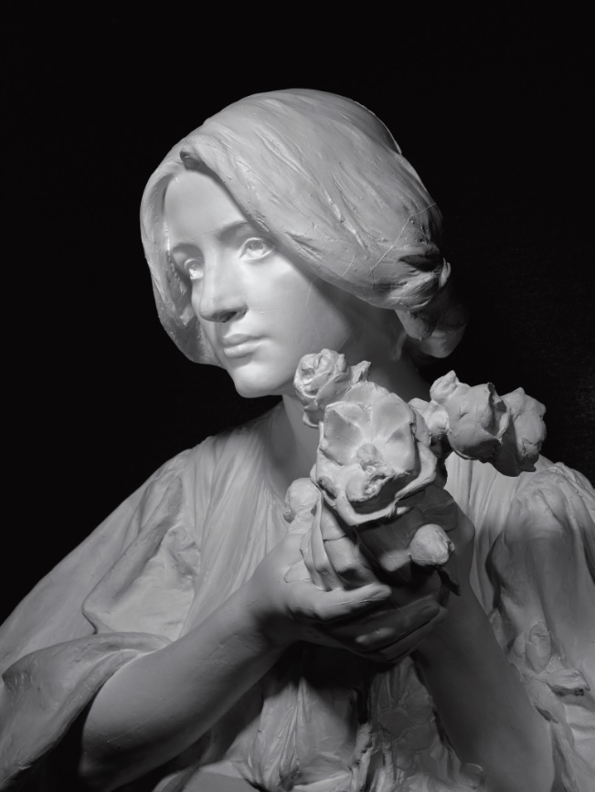 Escultura. Retrat de mig cos d'una noia amb un ram de flors a les mans
